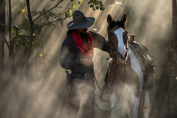 A cowboy leading his saddled horse through a dusty forest as sun rays stream through the trees