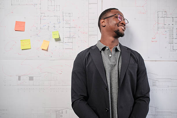 One smart young Black male architect in suit standing with design work on board, building construction blueprint with business concept ideas in studio company, happy and confident in presentation.