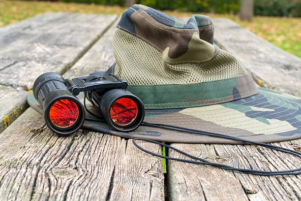 istock Camouflage hat and binoculars sitting on a rustic wooden picnic table in an outdoor setting 2248819157