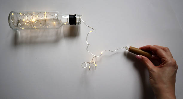 istock Glass bottle with a string of LED fairy lights partially pulled out by a hand holding the cork stopper. Photography. 2248822280