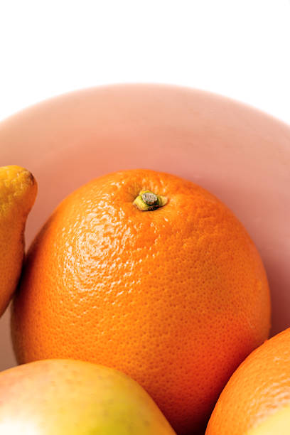 A ripe orange among fruits in a ceramic bowl