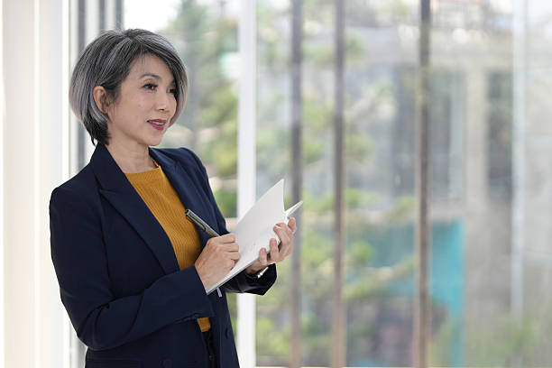 istock Asian older businesswoman noting ideas professional office setting working with focus planning future strategies making important decisions by window light 2248829191