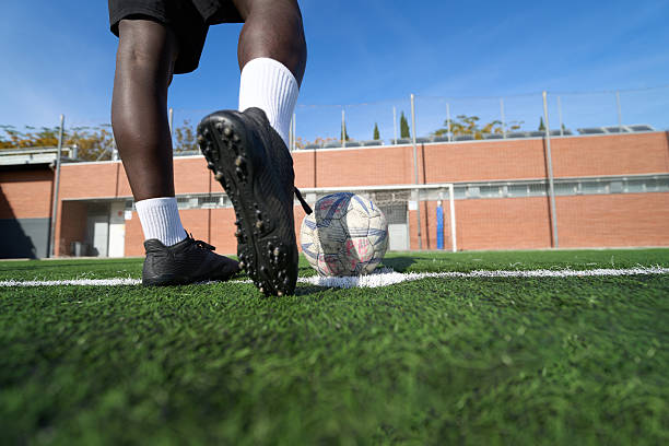 Athlete placing foot on soccer ball on a green turf field, preparing for a corner kick during a game or practice