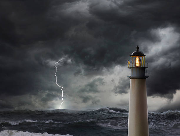 A lighthouse is silhouetted against a cloudy sky. The sky is dark and the lighthouse is the only light source
