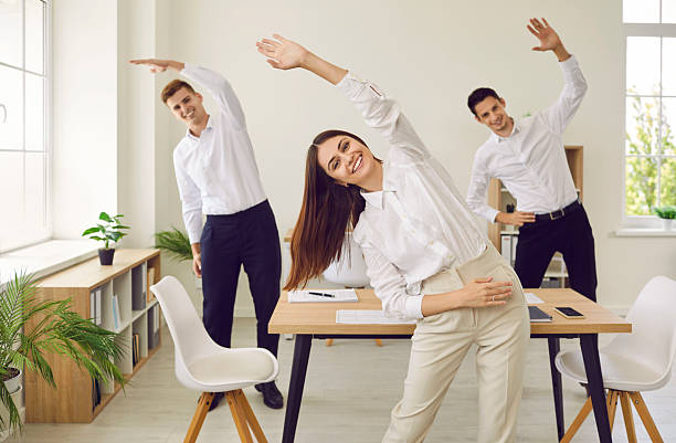 istock Happy smiling young business people doing stretching exercises in office on workplace. 2248837550