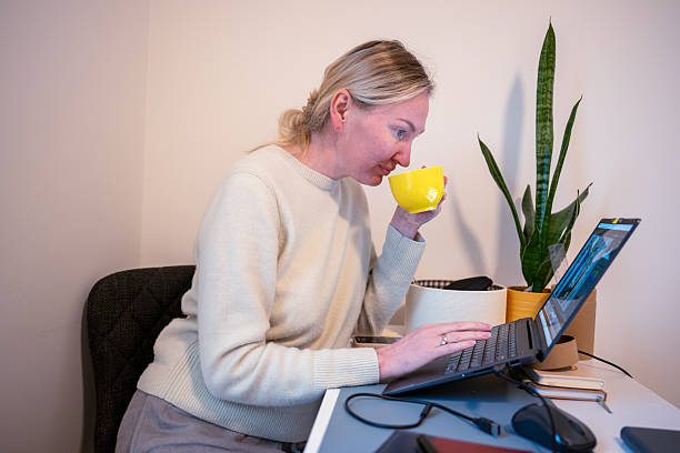 istock Woman drinking from mug while working on laptop at home office desk 2248838956