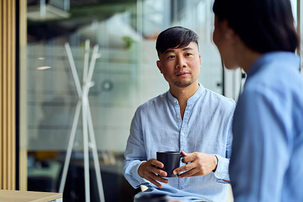 istock Asian Man In A Light Blue Shirt Holds Coffee While Chatting In Modern Office 2248839022
