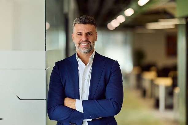 istock Confident Businessman In A Blue Suit Smiling While Leaning Against Glass In Modern Office 2248839042