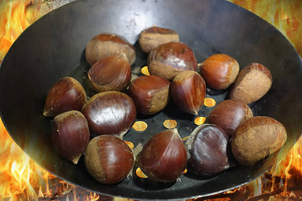 Roasted chestnuts being cooked in a perforated pan over a wood fire