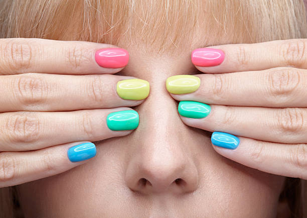 Closeup shot of young blonde woman with fun  varicoloured finger nails manicure.