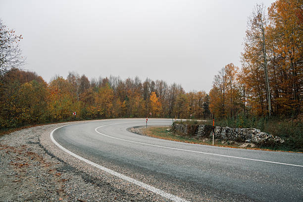 Curvy road in mountain area with falling off a cliff warning traffic sign.