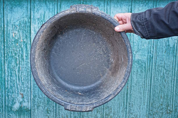 hand holding one black dirty old round plastic basin against green wall background on rural street