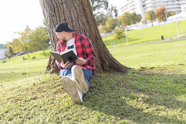 istock Man relaxing in park reading book under tree 2248851567
