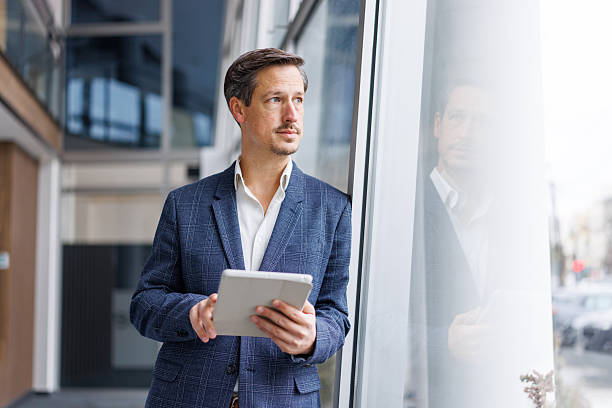 istock Thoughtful businessman holding digital tablet looking out office window 2248853573