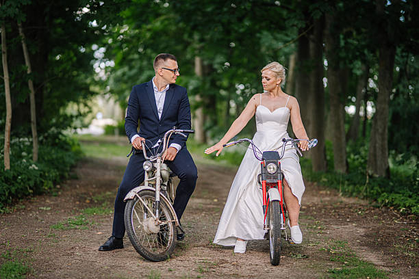istock Bride and groom in formal attire riding bicycles on a scenic path surrounded by trees, capturing a playful and romantic moment in nature with a joyful atmosphere 2248857262