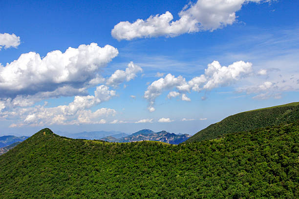 A picturesque mountain landscape featuring green hills and a clear blue sky with scattered clouds.