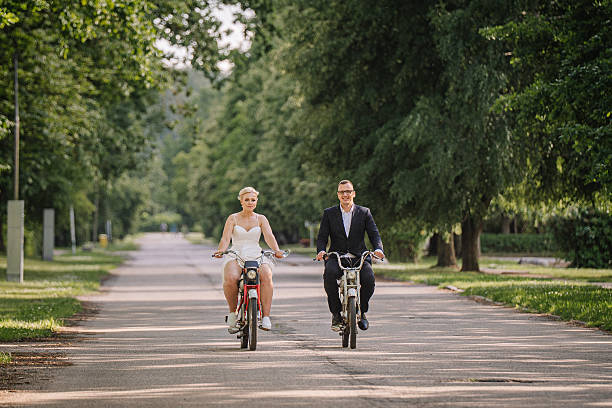 istock Couple riding bicycles on a tree-lined path, showcasing joy and connection, dressed in formal and casual attire, capturing a moment of togetherness and celebration 2248858004