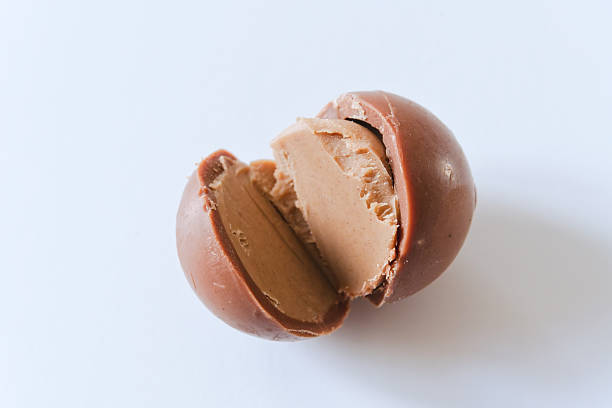 An artisan bonbon cut open to showcase its velvety filling, shot with natural light against a minimal white background. The centered composition and soft shadows enhance the quiet luxury of this sweet treat. Perfect for editorial, packaging, or design with available negative space.