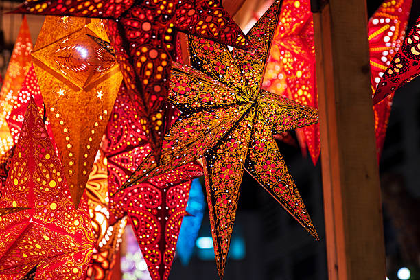 istock Vibrant star shaped lanterns in red, orange, gold patterns glowing hanging at a festive christmas market stall. Detailed perforated designs create sparkling light effects, 2248860786