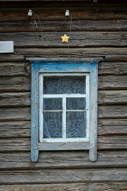 Old rural wooden facade with lace-curtained window and weathered texture