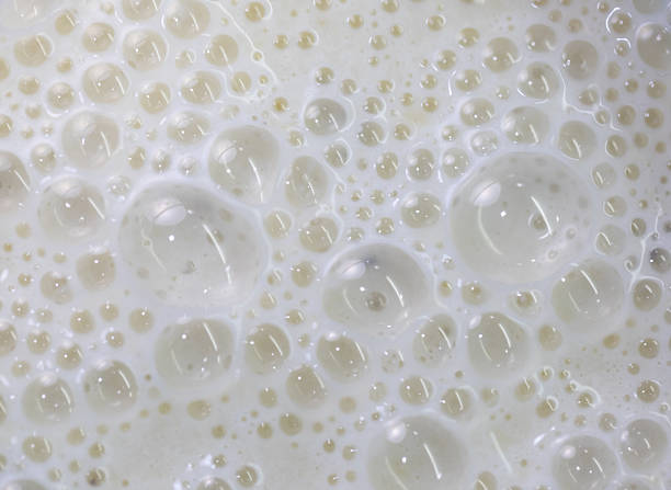 Macro close-up of white bubbles on a milky liquid. This abstract texture creates a clean and fresh background for food, cosmetic, or science-related themes.