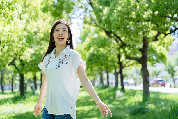 A cheerful woman runs through a sunlit green park, surrounded by vibrant trees and fresh greenery.The scene conveys a bright, refreshing atmosphere filled with positivity, freedom, and natural energy.Perfect for themes such as wellness, lifestyle, nature, outdoor activities, and refreshment.