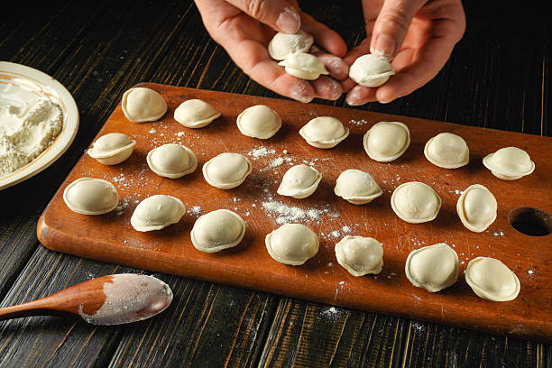 istock In a warm kitchen, hands are skillfully shaping dumplings on a wooden board sprinkled with flour. The process highlights the care in traditional cooking 2248876047