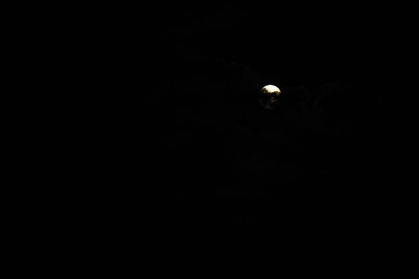 A luminous full moon is visible in a night sky filled with dark clouds. The moon's glow creates a contrast against the darkness, illuminating the scene softly.