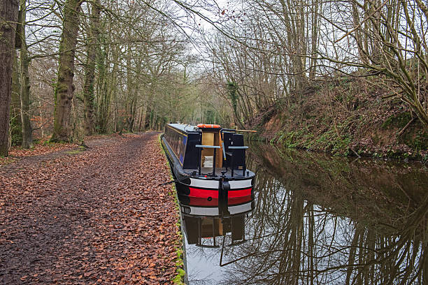 Narrowboat moored up in English rural countryside scenery on British waterway canal with trees and leafy towpath in winter