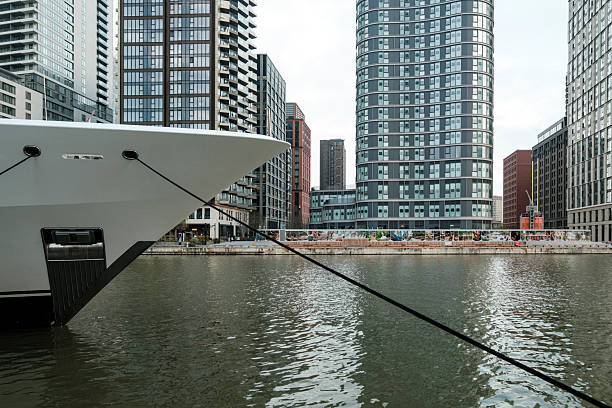 Luxury yacht moored in a vibrant urban harbor, reflecting modern architecture and the contemporary financial cityscape of canary wharf under an overcast sky, symbolizing wealth and urban lifestyle