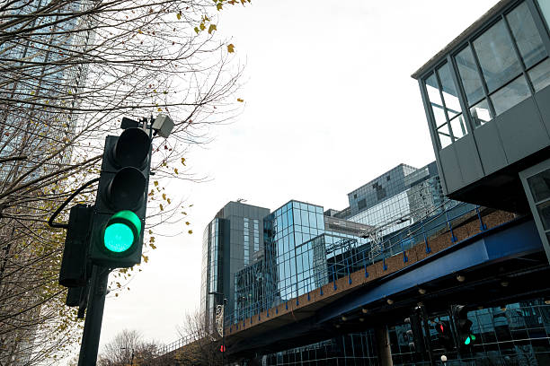 Traffic light with a green signal indicating go, set against a backdrop of modern glass buildings and an elevated railway structure in an urban city environment