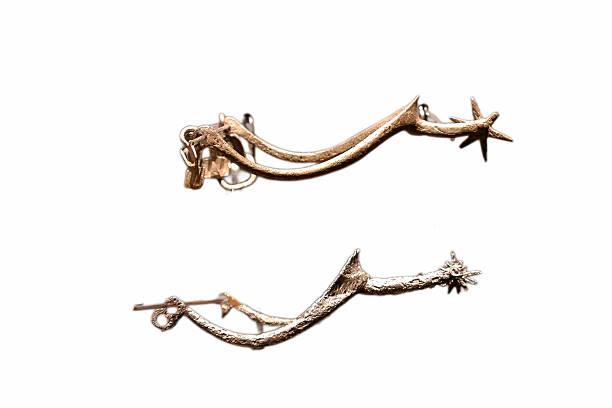 An antique pair of spurs rests on a white surface. These spurs feature a detailed design with star shaped ends, reflecting the art of metalworking and history.