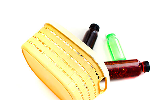 A yellow plastic basket sits beside bottles of red green and brown liquid on white