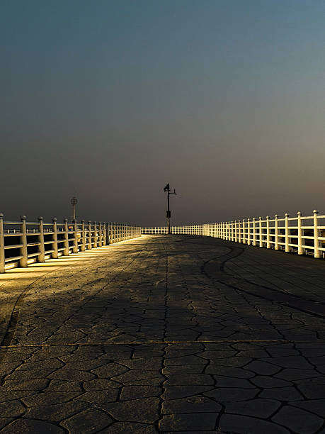 Pier walkway stretching into the distance at twilight, streetlights casting long shadows and creating a peaceful ambiance