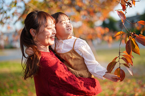 istock Mother Holding Child While Looking at Autumn Leaves in Park 2248895681
