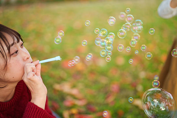 Soap bubbles floating through the air as an adult blows bubbles outdoors, captured against a soft autumn background. Playful lifestyle image emphasizing movement, lightness, and simple joy with shallow depth of field and natural daylight.
