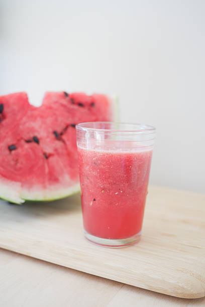 Refreshing watermelon juice placed beside a sliced watermelon on wood.