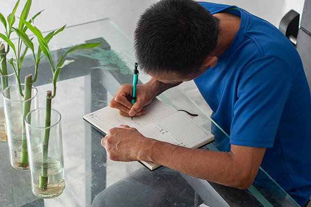 istock Top view of a man leaning over a glass table writing in a notebook, focused, with visible amputation of his left fingers. 2248899631