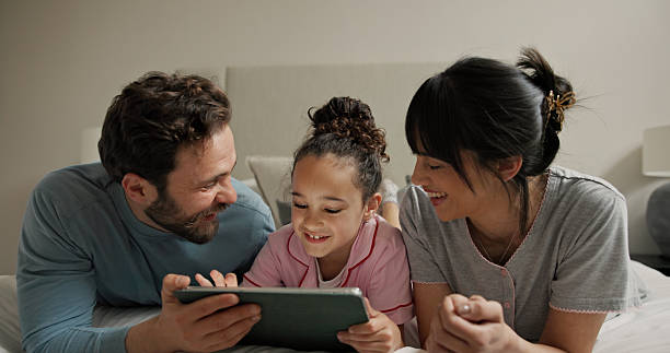 istock Parents, girl and tablet in bed, smile and bonding with online games, scroll or problem solving in home. People, mother and daughter with dad, tech and relax with app for puzzle at family house 2248902225