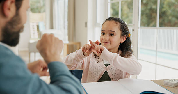 istock Dad, kid and learning sign language in home for development, growth and care in homeschool. Education, father and teaching student asl, hand gestures and happy girl with hearing disability in house 2248902304