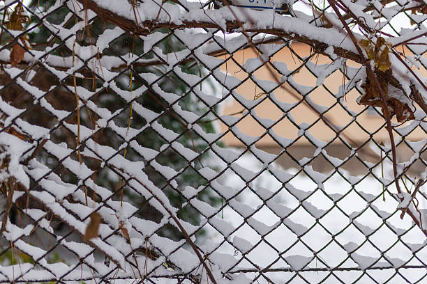 A chain-link fence coated with evenly fallen snow forms a striking geometric winter pattern. The delicate lattice creates a calm seasonal backdrop perfect for holiday, outdoor, or minimalist winter concepts.