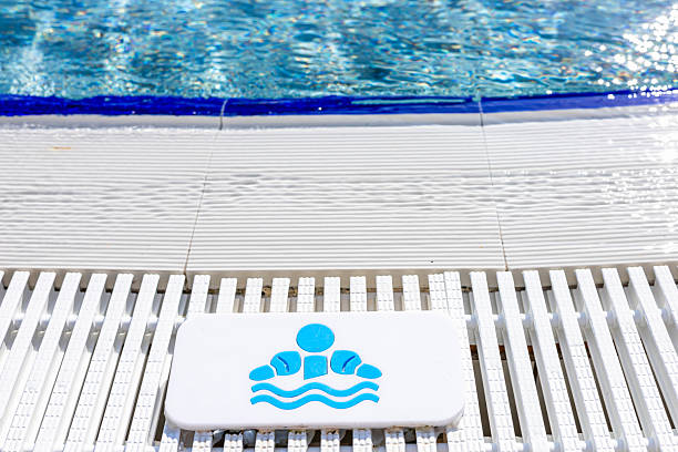A swimming pool with clear blue water and a white deck. A sign indicating swimming rules for children is visible near the edge of the pool.
