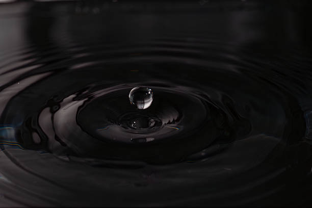 239.Droplet hovers above water forming concentric ripples. Low lighting and reflections highlight fluid motion, surface tension, and wave propagation.