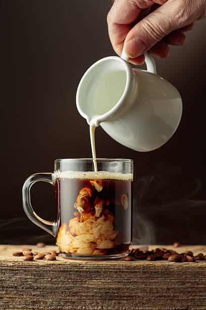 Coffee in a clear glass mug with cream being poured.