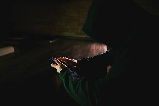 istock Hooded person using a glowing device in darkness 2248919775