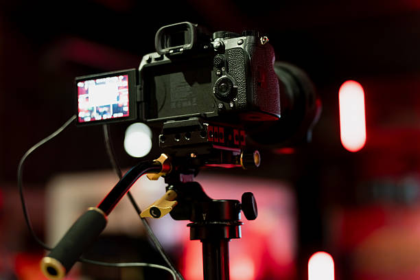 istock Professional camera rig on tripod showing active side monitor, control buttons and attached lens in dim studio environment with glowing red light accents 2248920703