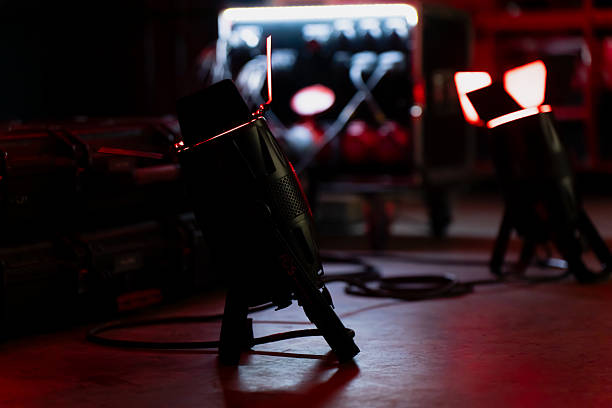 istock Ground-level view of two professional stage lights emitting focused red light from their opened barn doors, set among cables and technical equipment cases inside a low-lit workspace 2248920762