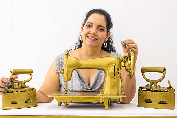 A Hispanic seamstress stands in front of an old sewing machine and iron, looking at the camera against a white background in Neiva, Huila, Colombia. Concept of businesswoman and copy space