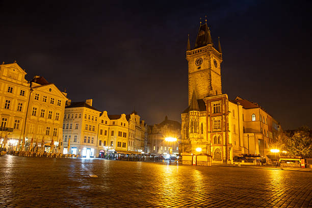 Prague old town square at night featuring the illuminated astronomical clock on old town hall tower and historic buildings under a dark sky, evoking a travel and european city destination