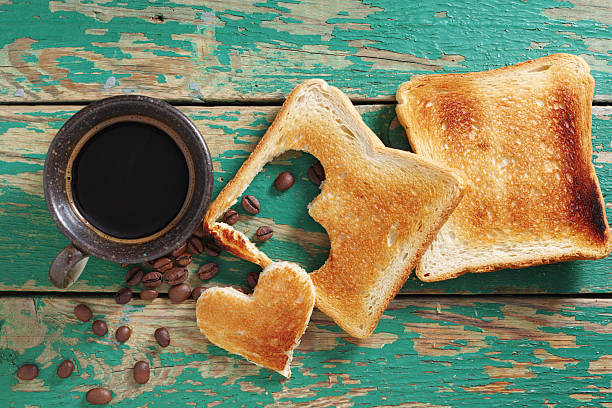 Cup of coffee and toast with heart-shaped cutout on old green wooden background, top view